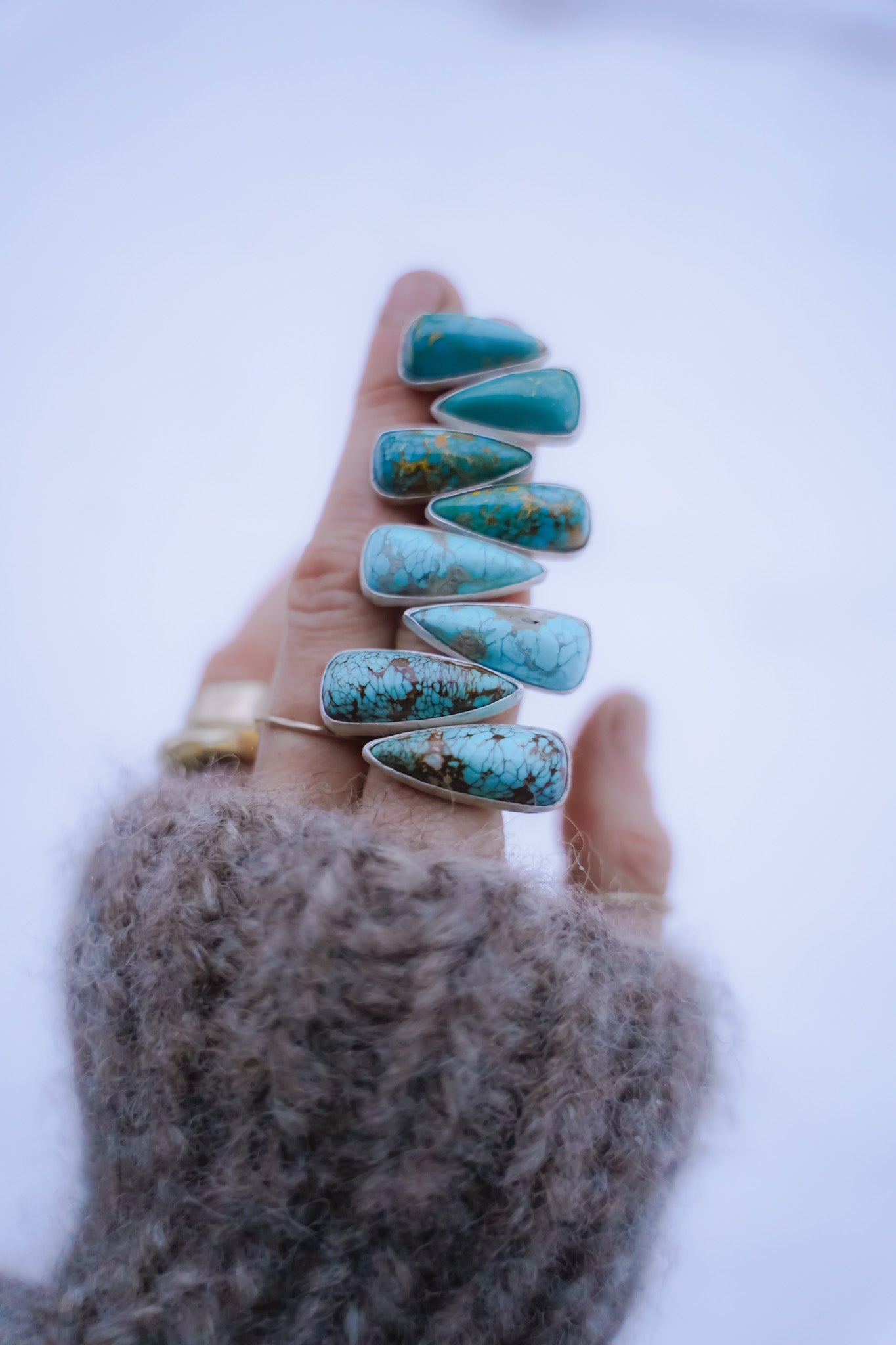 A woman's hand against a white background holding four pairs of spike-shaped turquoise and sterling silver earrings. They range in size from long to short.