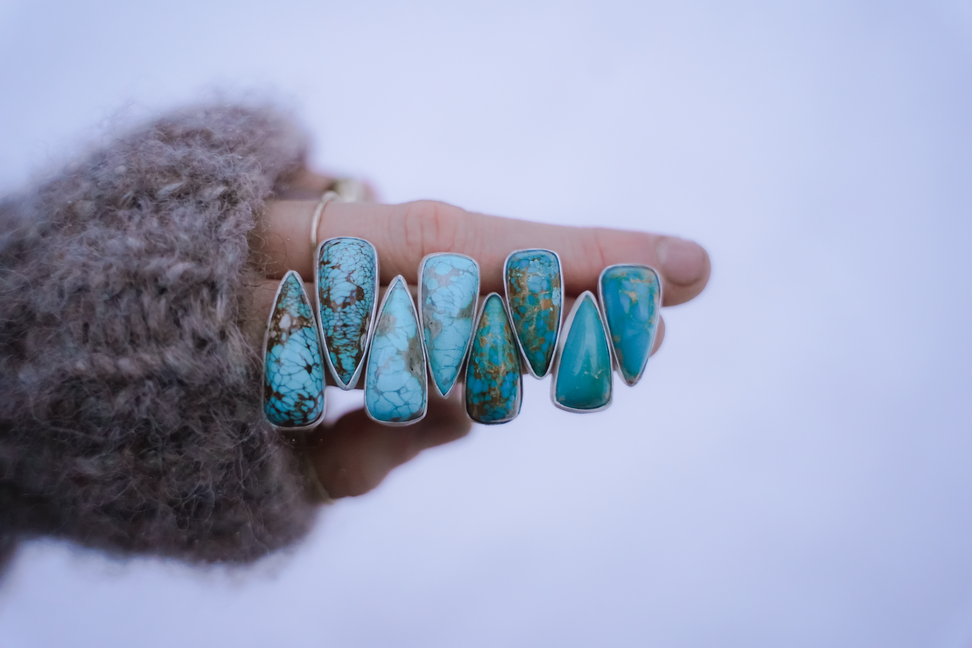 A woman's hand against a white background holding four pairs of spike-shaped turquoise and sterling silver earrings. They range in size from long to short.