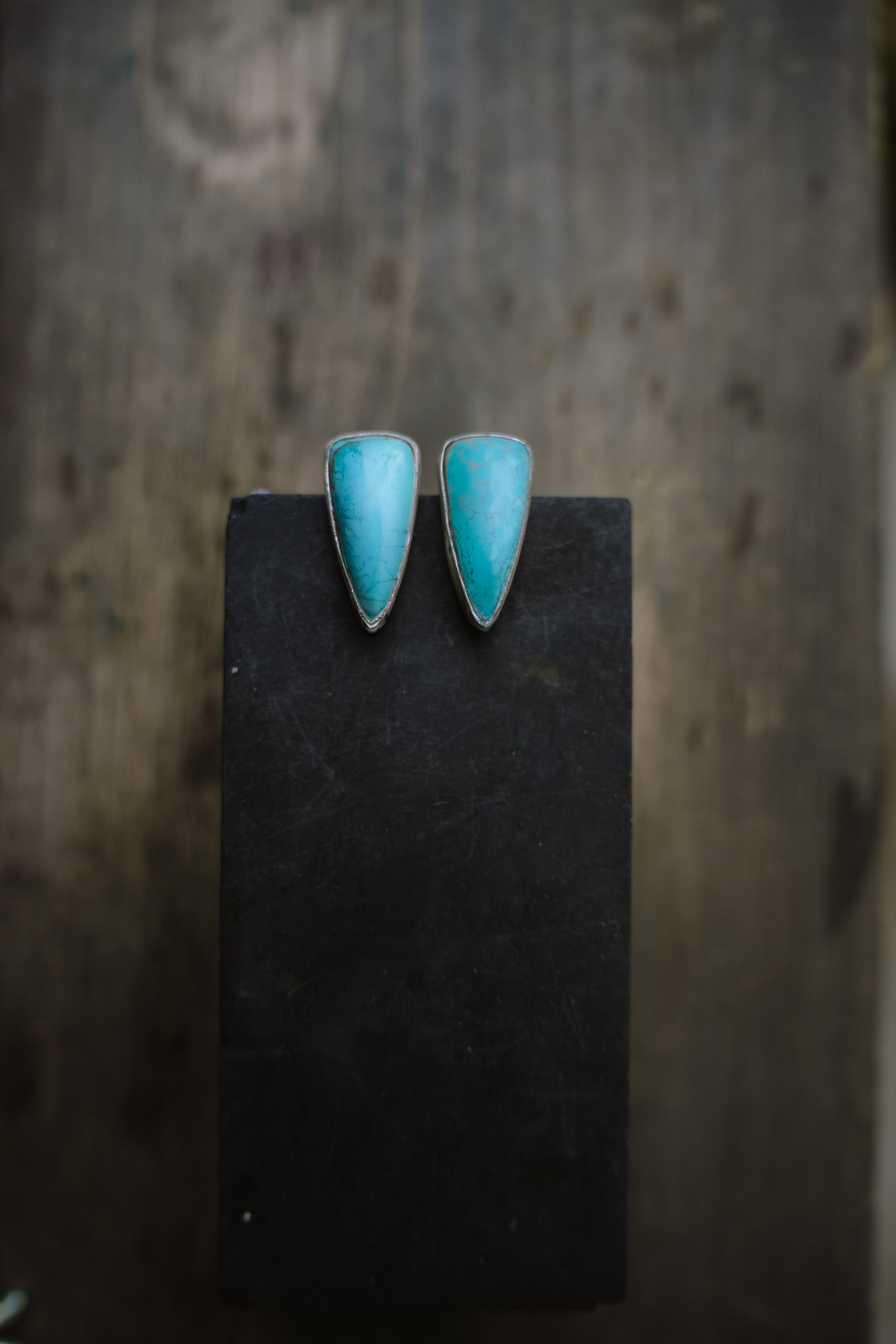 A pair of turquoise spike-shaped earrings set in sterling silver against a blurred, natural background.
