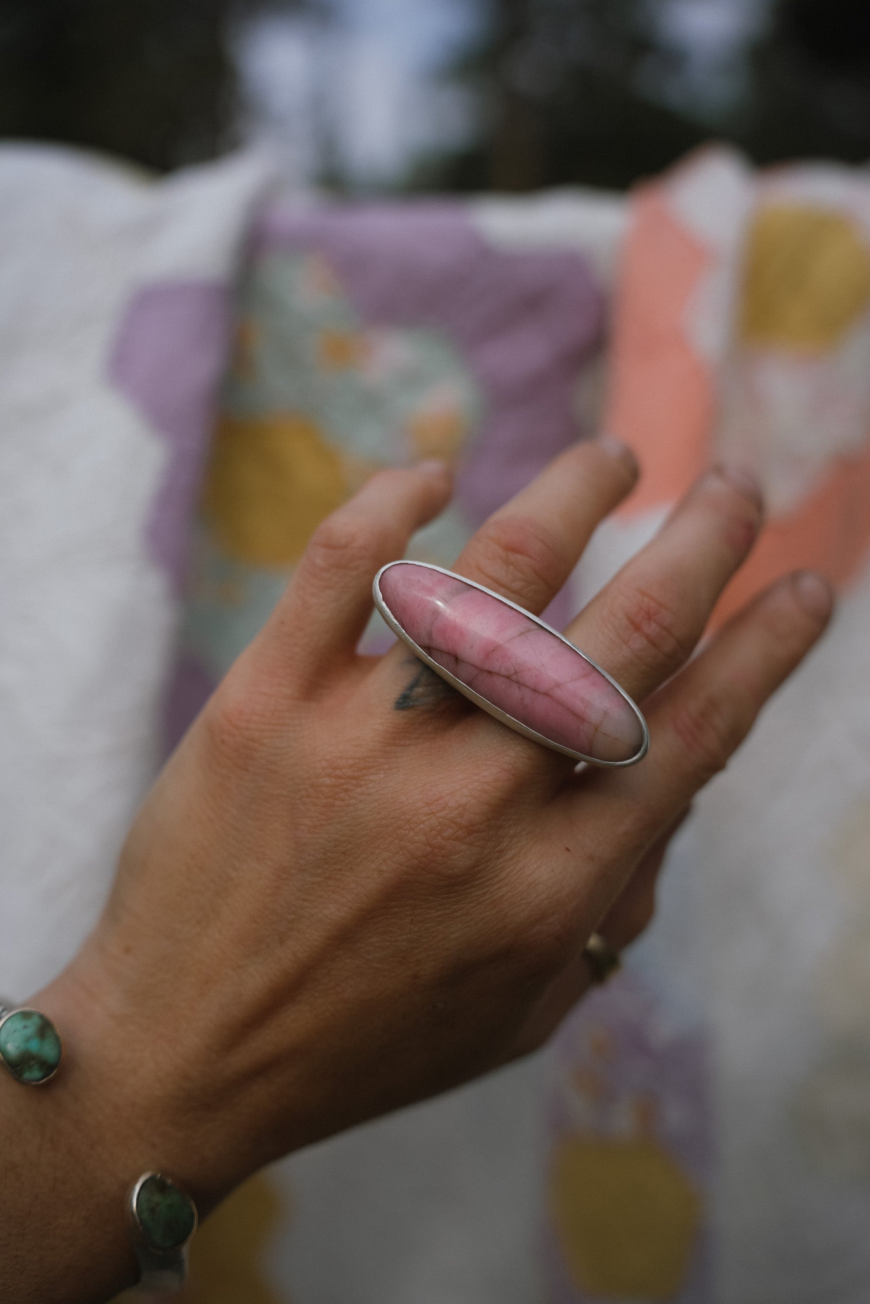 A woman's hand wearing a two-fingere pink stone ring with a blurred background