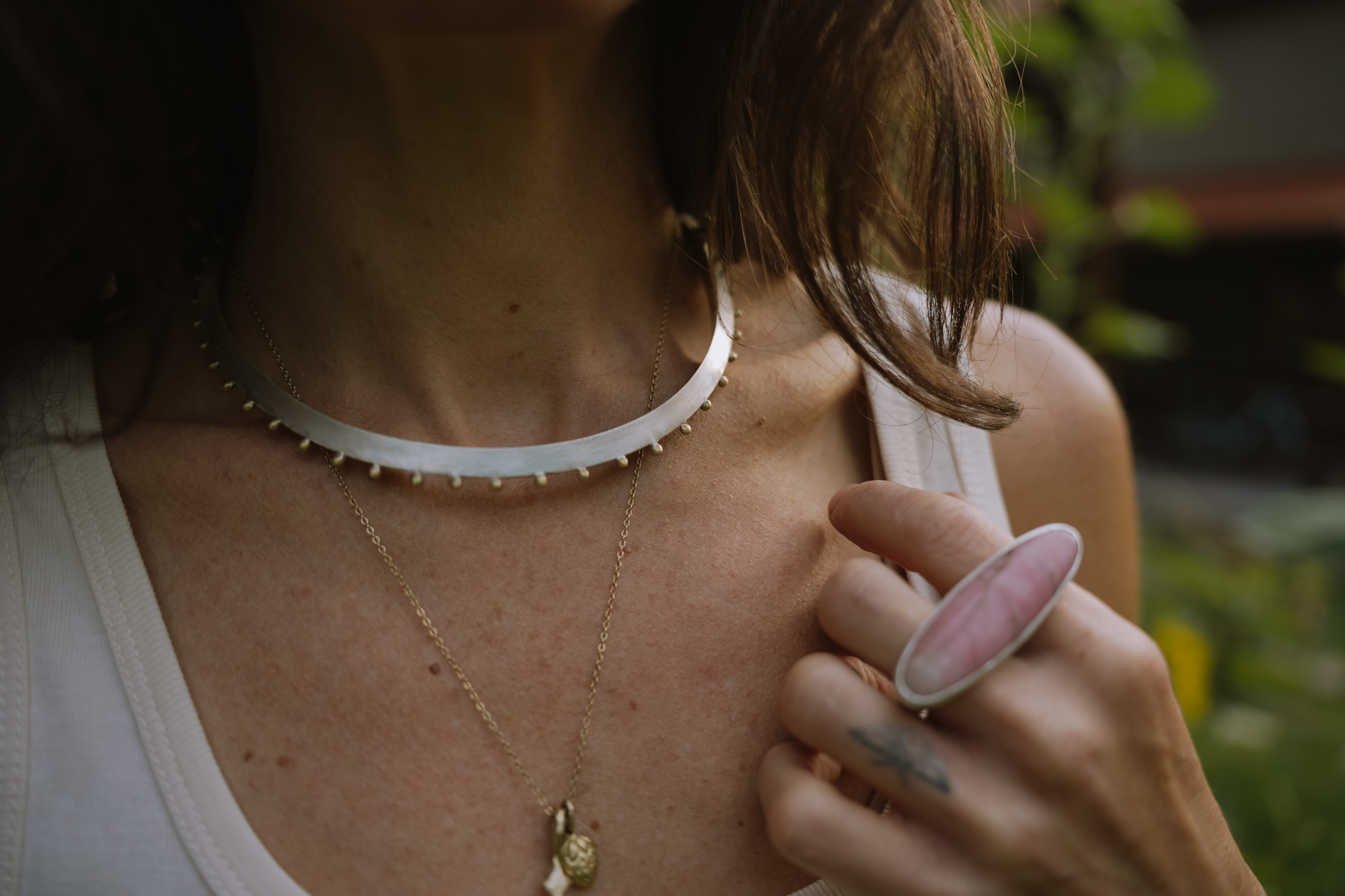 Close-up of a person wearing a silver choker, and a two-fingered pink rhonodonite and silver with a blurred background