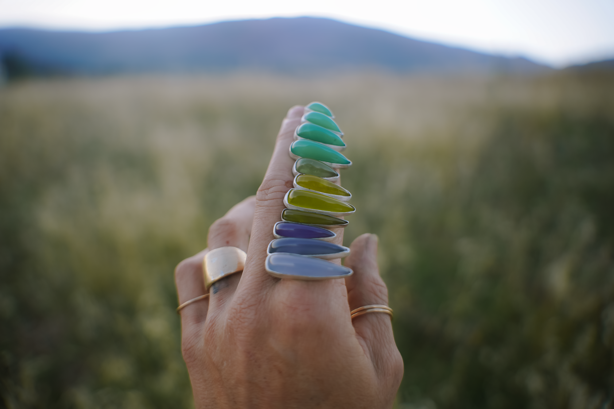 A woman's hand balancing six pairs of spike-shaped sterling silver and vesuviante post earrings of varying colors, from green to purple.