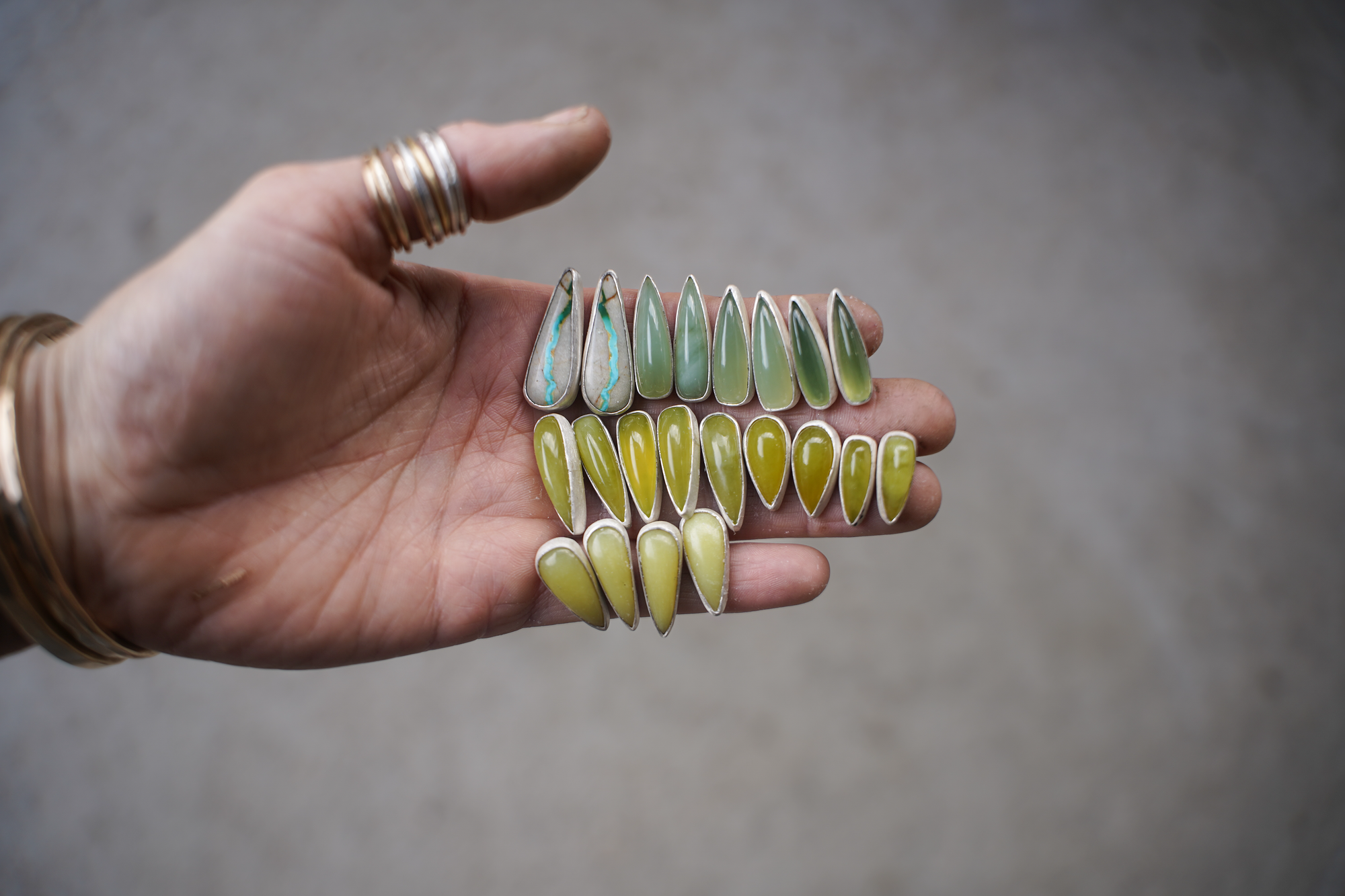A woman's hand holding ten pairs of spike-shaped sterling silver and vesuviante post earrings.