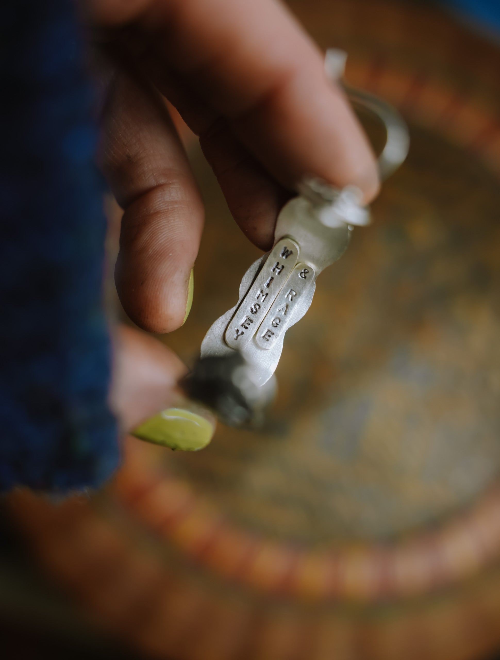 A woman's hand holding a sterling silver hoop earring and showing the underside which is stamped with "Whimsy & Rage."